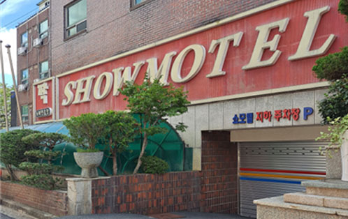 빨간바탕에 흰색글씨로 쇼모텔이 영문으로 적혀 있으며 지하주차장이 보이는 모습