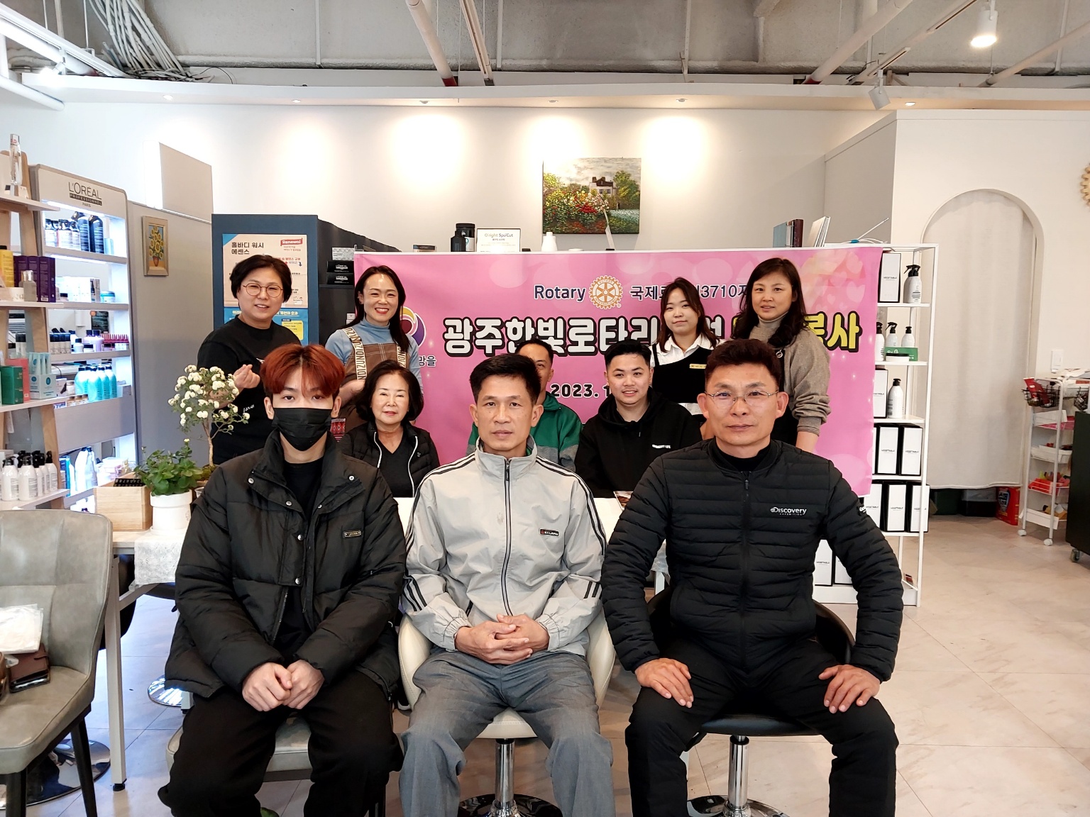 11월19일 미용봉사 후 단체 사진 촬영, 남성 3명이 앞 쪽 의자에 앉아서 포즈를 취하고 있다. 