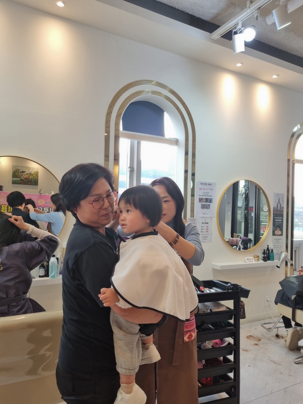 11월19일 미용봉사 중인 사진. 한 여성이 아이를 안고 있고 다른 한 여성이 아이의 머리를 손질하고 있다.
