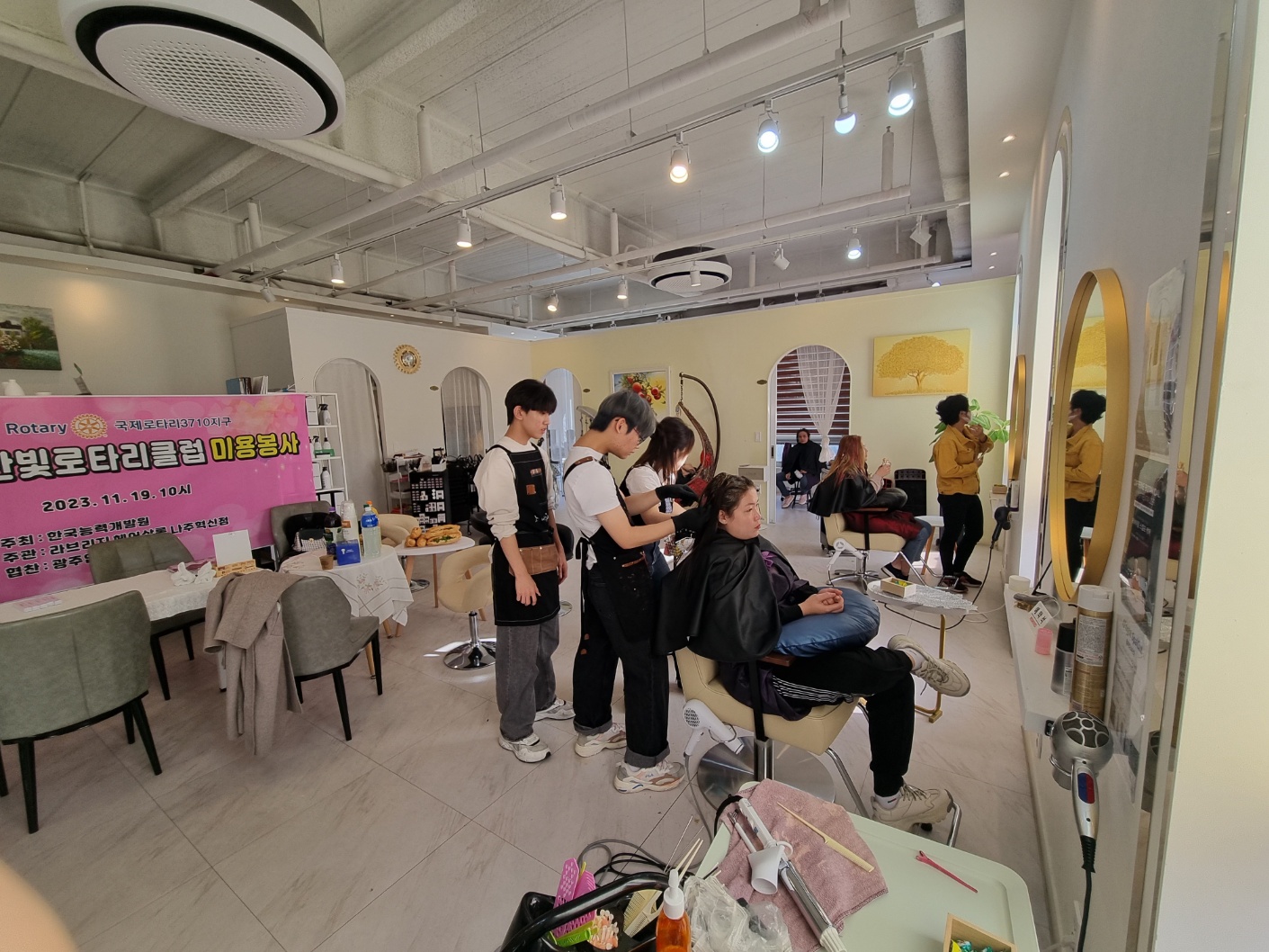 11월19일 미용봉사 중인 사진. 한 남성이 여성의 머리를 손질하고 있고 다른 남성이 이를 지켜보고 있다.